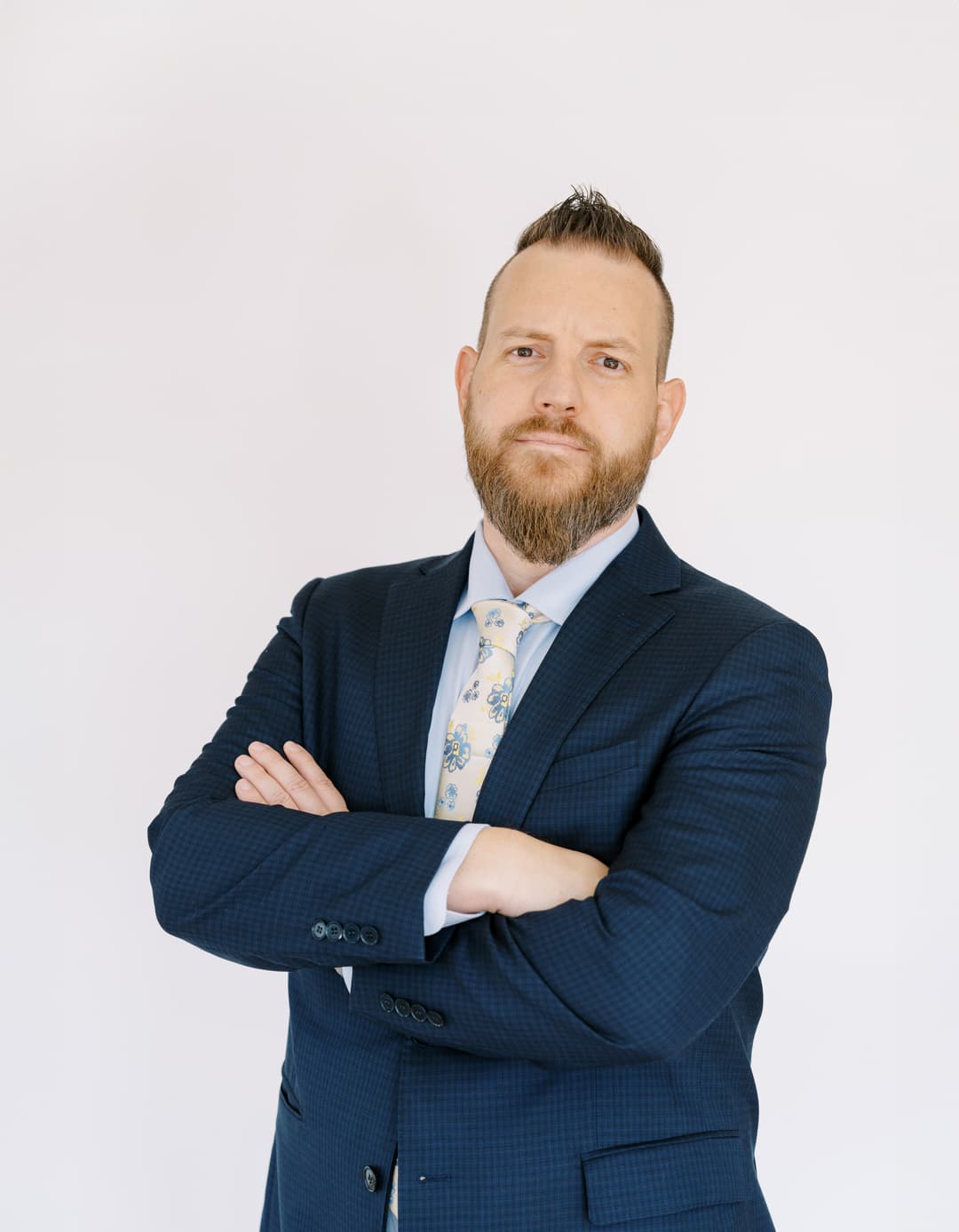Confident business professional in a navy suit with arms crossed, standing against a plain background.